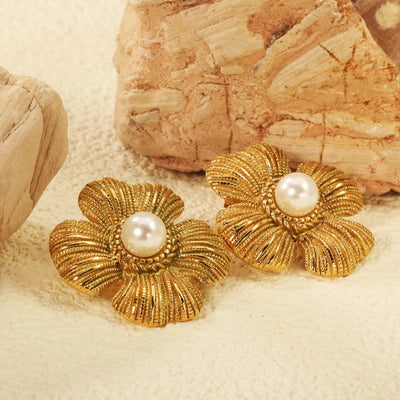 Close-up of 18kt gold-plated vintage flower pearl earrings resting against warm sandstone textures, highlighting rich ribbed petals and beaded detail.