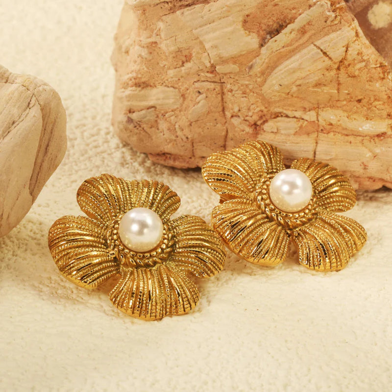 Close-up of 18kt gold-plated vintage flower pearl earrings resting against warm sandstone textures, highlighting rich ribbed petals and beaded detail.