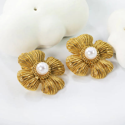 Angled view of textured gold flower stud earrings with luminous faux pearls, displayed on an ivory stone backdrop for added dimension.
