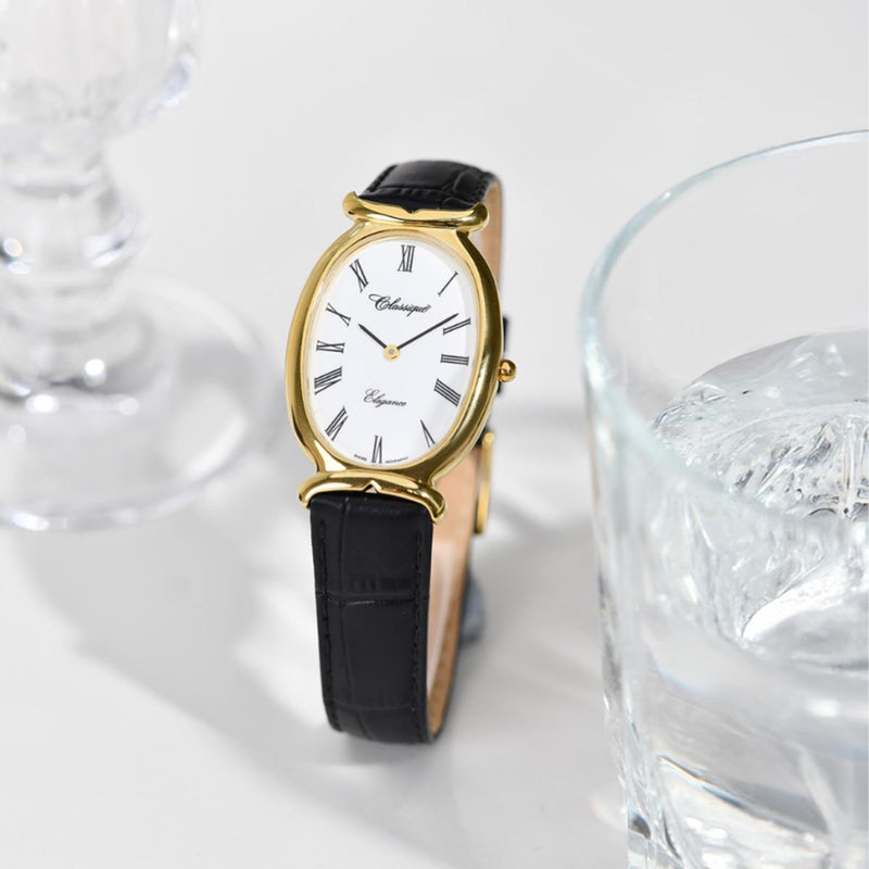 Captured next to a glass of water, the Classique Oval Ladies’ Watch reflects timeless beauty. The gold-plated stainless steel case and bold oval face shimmer elegantly, while the camel black leather strap adds a sophisticated contrast.