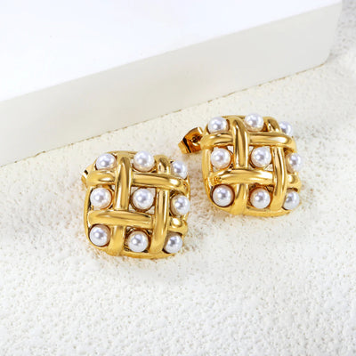 Angled view of square gold lattice studs with pearl accents, resting on a white block to show depth and glossy finish.