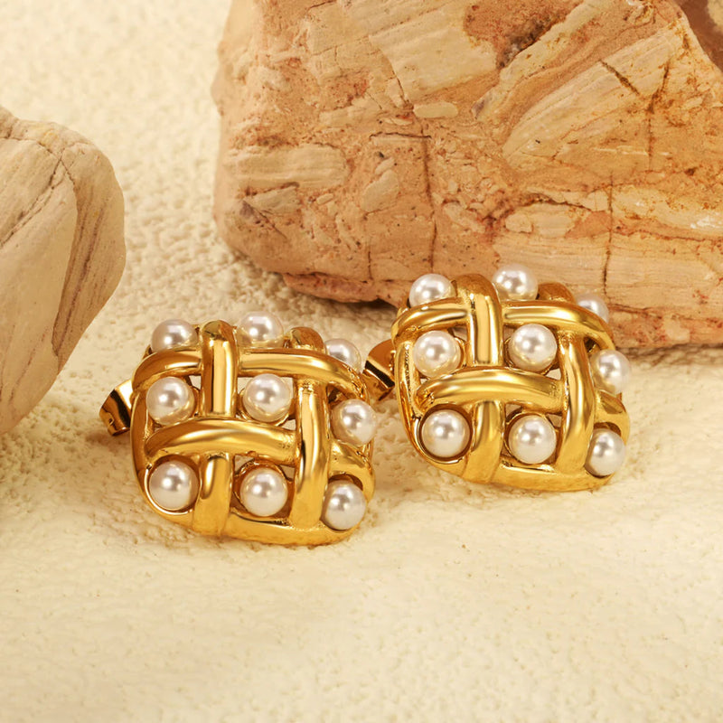 Lifestyle shot of gold-plated woven lattice pearl earrings nestled against warm sandstone, highlighting their rich sheen and sculptural form.
